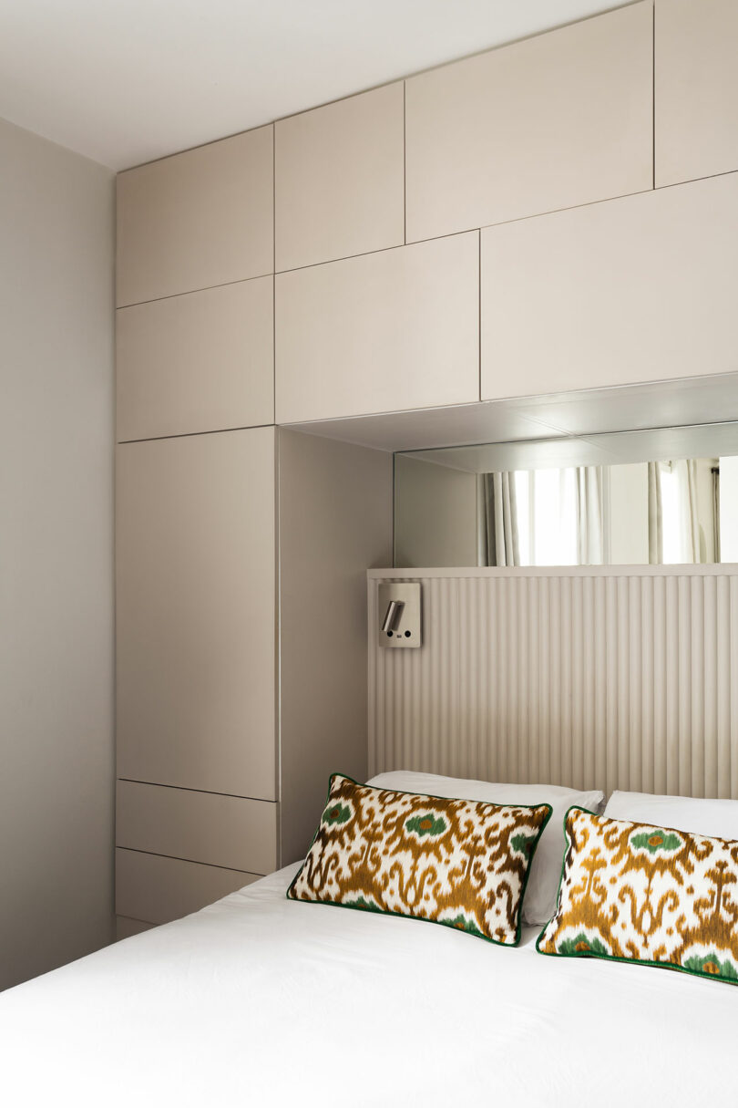 A bedroom view showing a large mirror mounted above a custom headboard to reflect natural light and create an illusion of space.