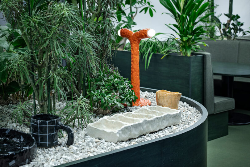 A small indoor garden with white gravel, ceramic objects, and an orange Y-shaped lamp.