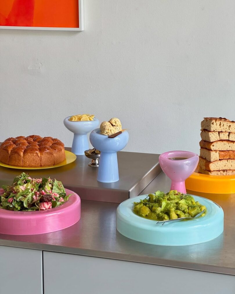 A bright table setting with pastel-colored glass plates and bowls filled with various foods like pasta and salad.