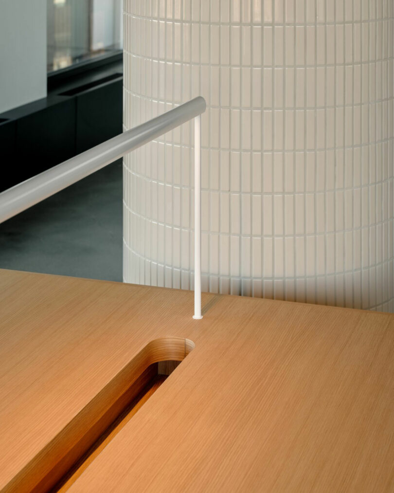 Close-up of a white vertical railing intersecting a custom wooden tabletop next to a tiled cylindrical column.