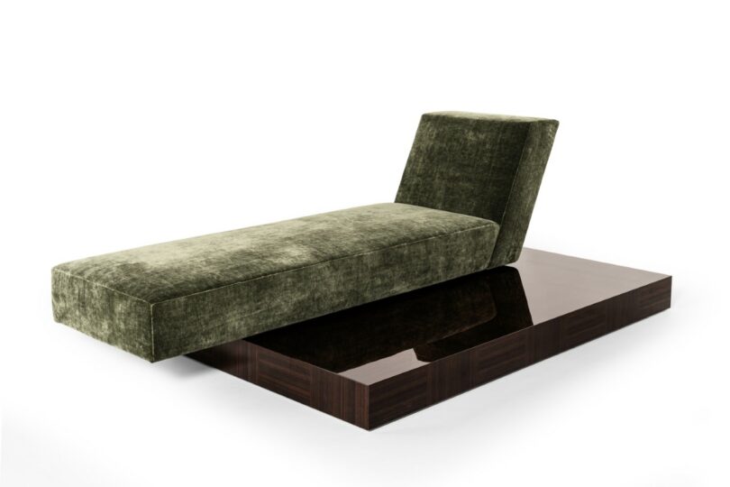 A sleek olive-green velvet chaise longue with a dark, polished wooden platform base against a white background.