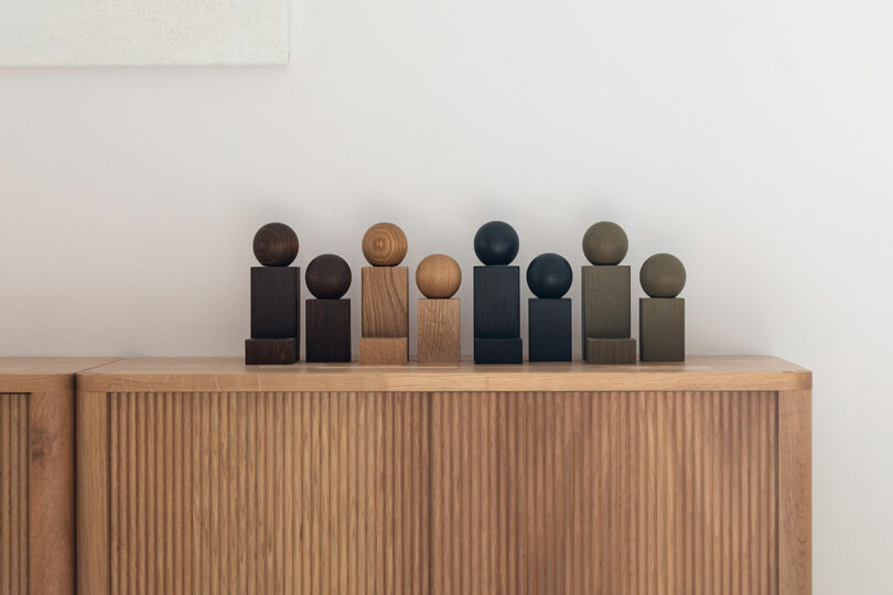 A collection of wooden geometric grinders arranged as art pieces on top of a minimalist wooden cabinet.
