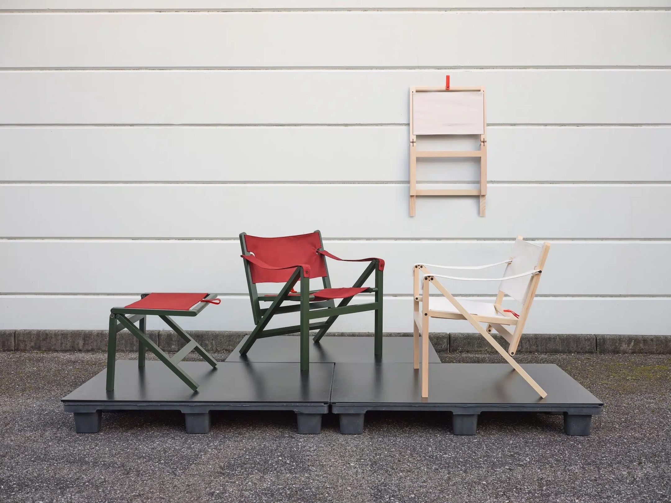 Three collapsible chairs folded completely flat and hung on a wall using integrated leather loops.