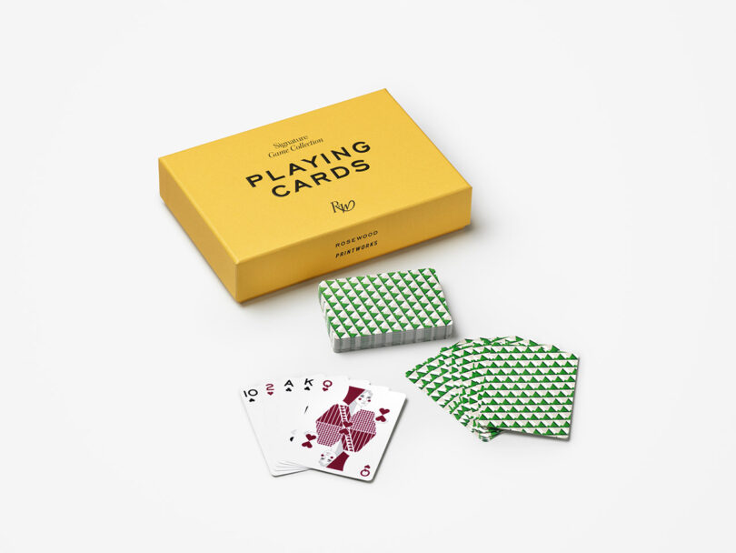 Designer playing cards with geometric patterns spread out next to their yellow box.