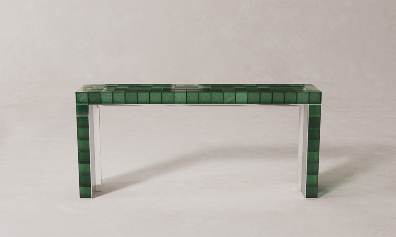 A minimalist rectangular console table with a green tiled top and sides and transparent legs.