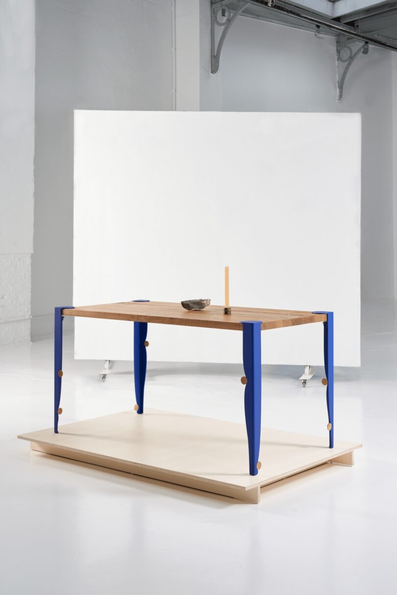 Minimalist wooden tabletop paired with vibrant blue Tiptoe legs in a bright white room.