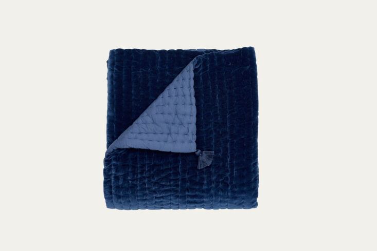 A quilted velvet throw blanket in a deep blue tone, showing its plush texture.