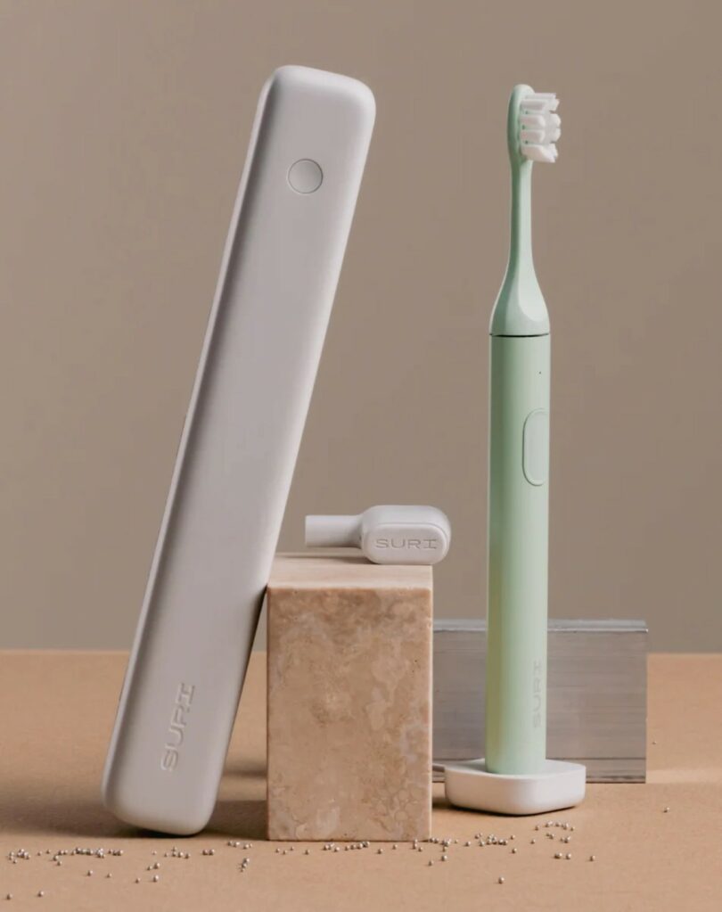 A mint green SURI electric toothbrush and its UV-C travel case artfully arranged on a beige surface.