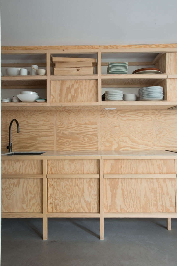 Detail of pine plywood cabinetry contrasted with a luxury marble countertop and black matte hardware.