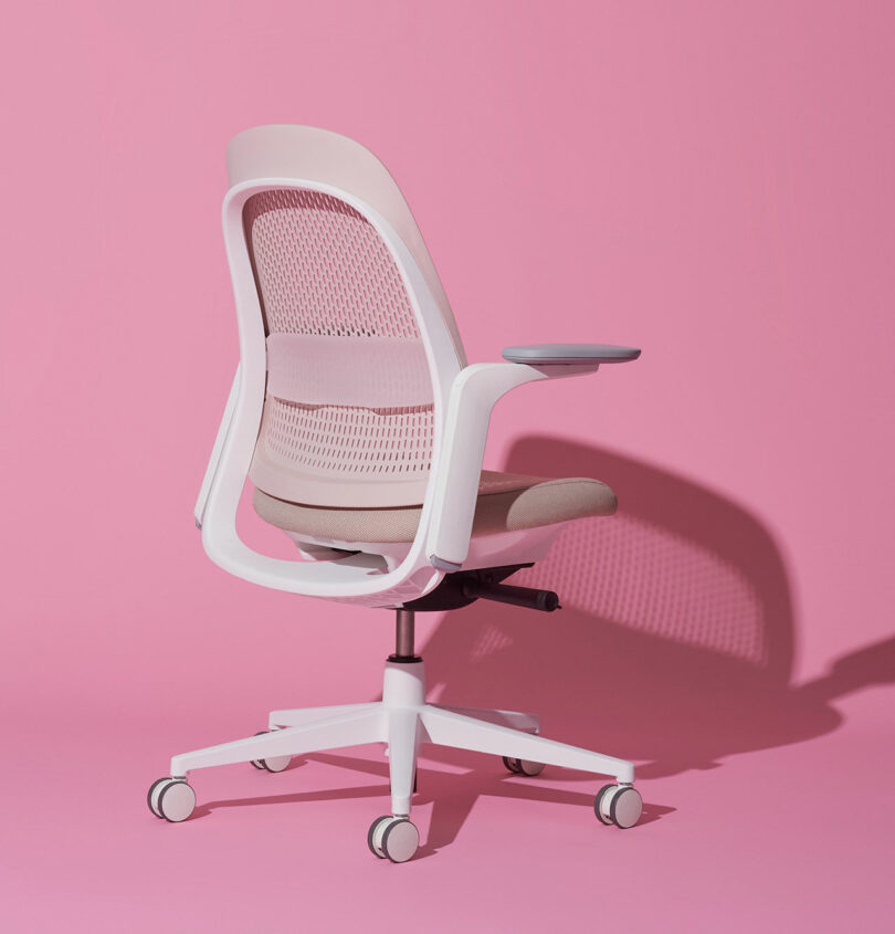 An ergonomic chair with a pink background, highlighting the recycled mesh and padded seat.