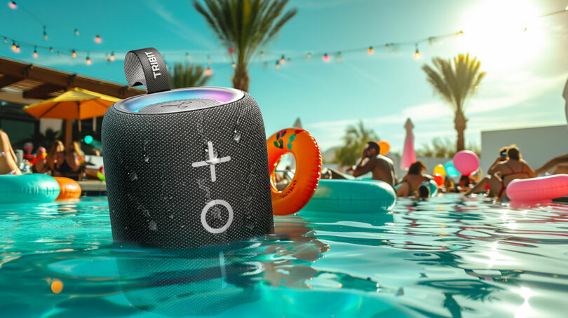A TRIBIT waterproof speaker floating in a swimming pool during a lively evening party with lights.