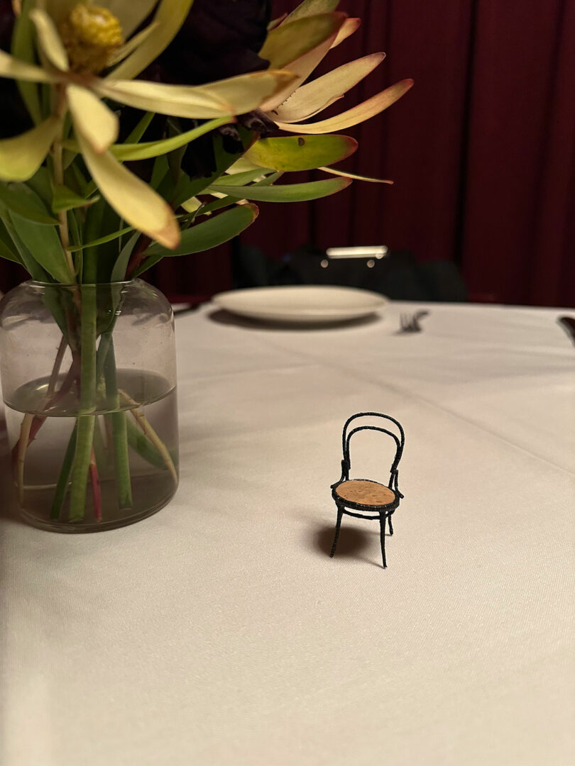 A miniature champagne chair placed elegantly on a dinner table next to a vase.