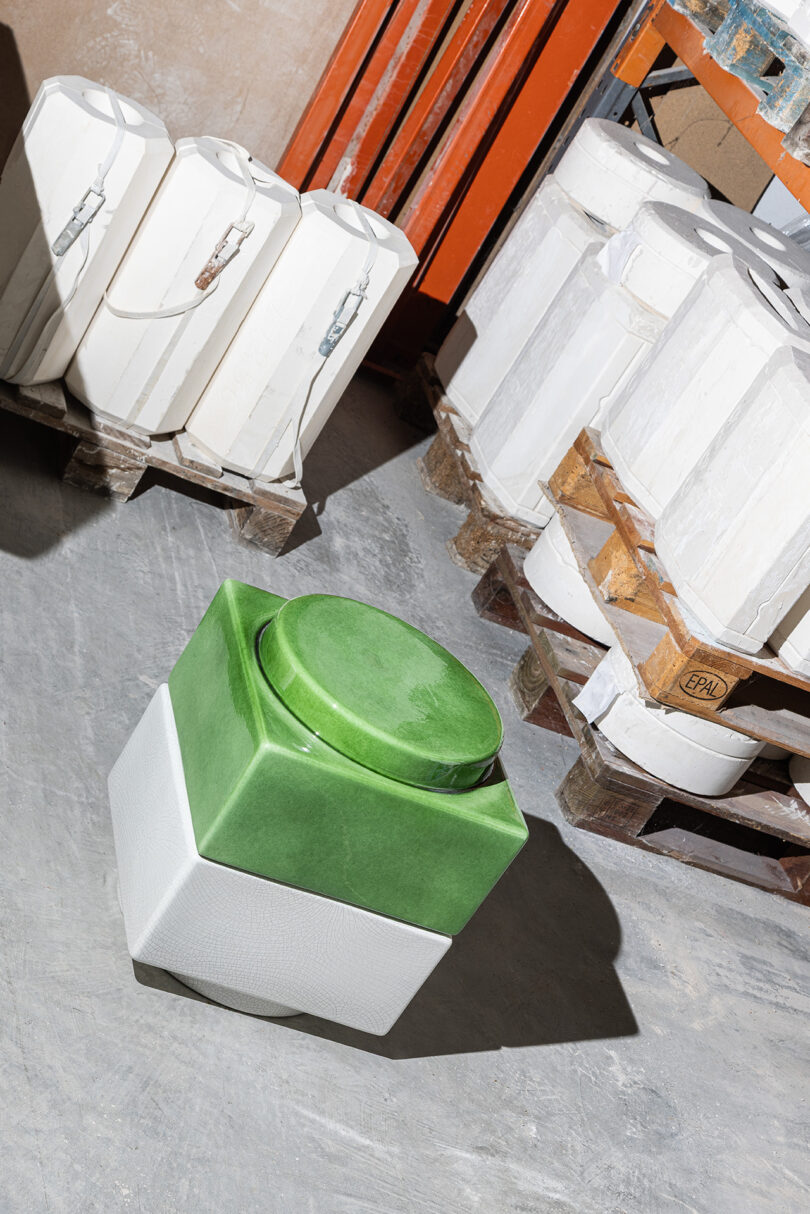 A green and white geometric vessel sitting near stacked industrial ceramic molds.