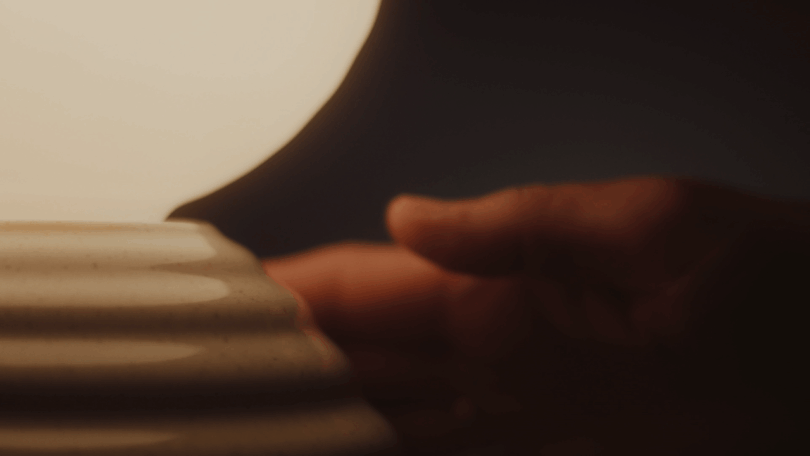 Close-up of a person's hand touching the ribbed ceramic texture of a glowing lamp base.