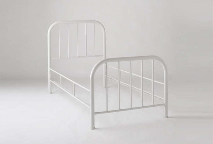 A white wrought iron bed frame in a minimalist setting.