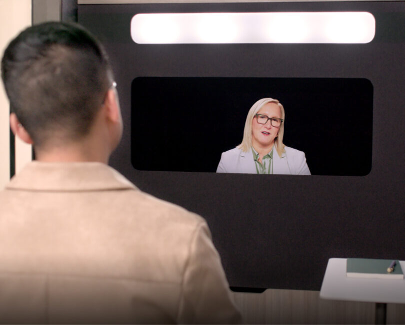 View from behind a participant looking at a woman in professional attire on a high-resolution Ocular View screen.