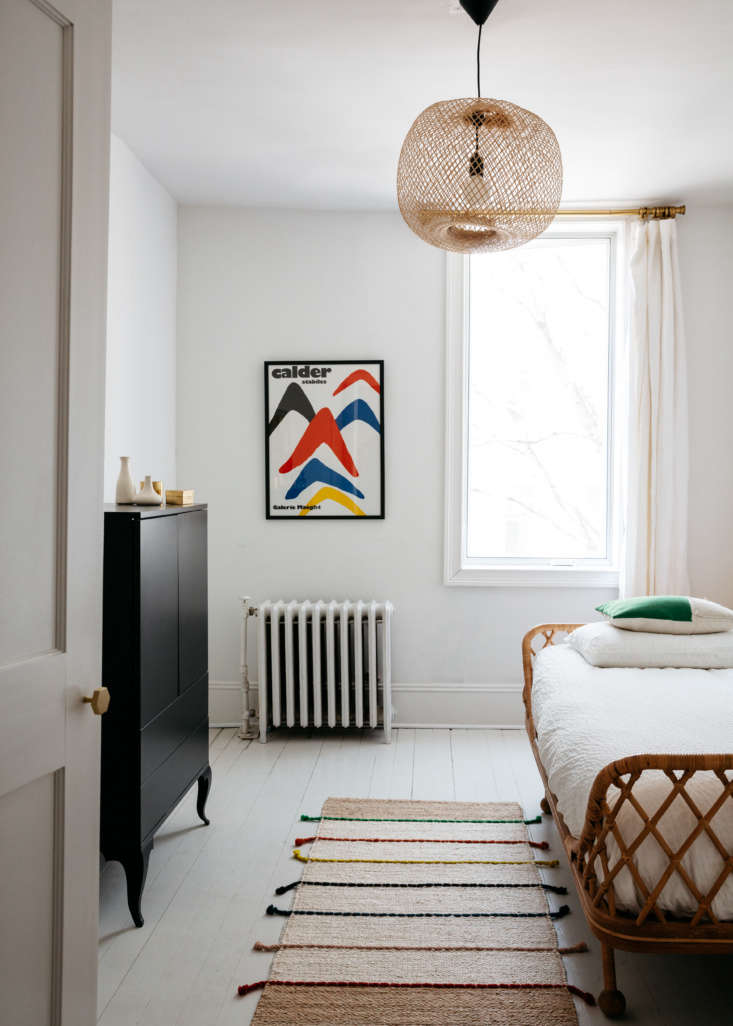 Wide shot of a minimalist guest room with high ceilings and natural light in a renovated townhouse.