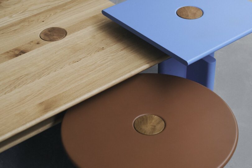 Three overlapping geometric tabletops in wood, blue, and brown finishes with circular accents.