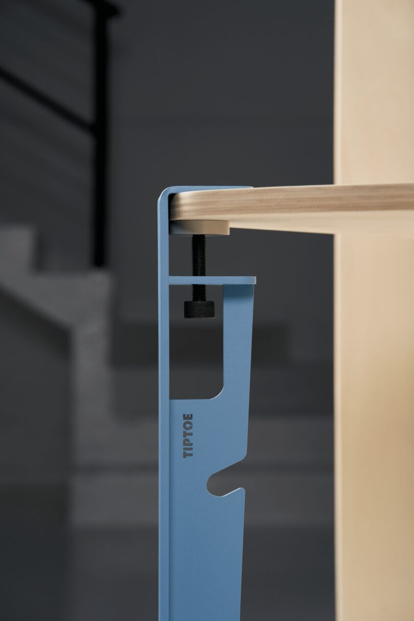 Macro shot of a blue Tiptoe metal clamp securing a wooden tabletop.