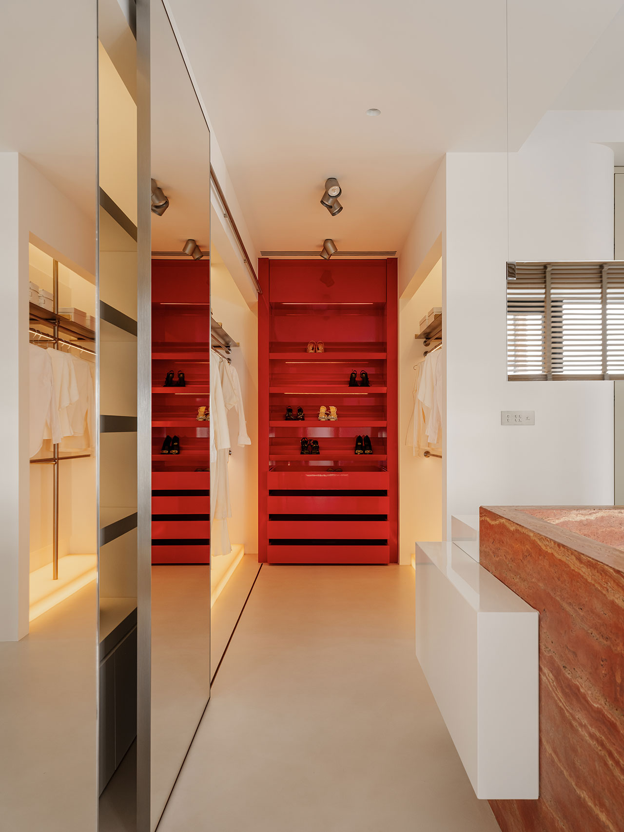 Modern walk-in closet with red shelving, organized clothing racks, and integrated lighting.
