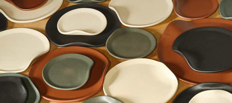 Assorted ceramic plates in earthy tones with irregular, organic shapes on a wooden surface.