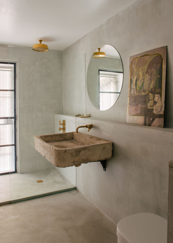 Microconcrete shower room with unlacquered brass fixtures and a vintage limestone sink.