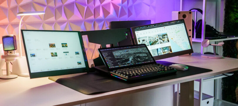 A modern white desk setup with multiple monitors and ambient RGB lighting.