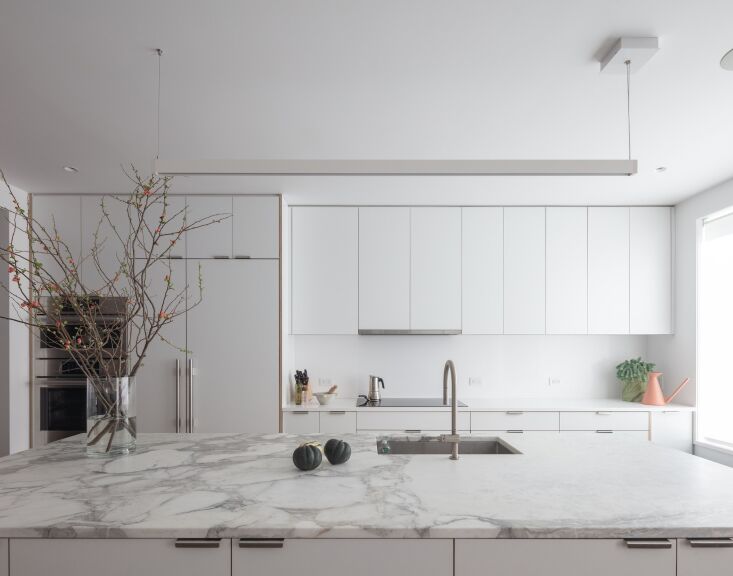 A large marble kitchen island with custom wood cabinetry and modern pendant lighting.