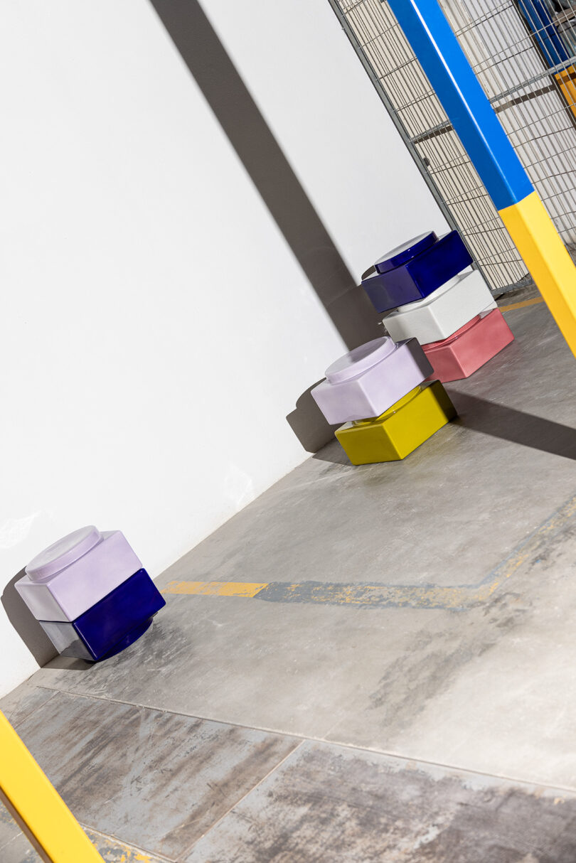 Three tall stacks of colorful geometric ceramic stools and containers against a industrial wall.
