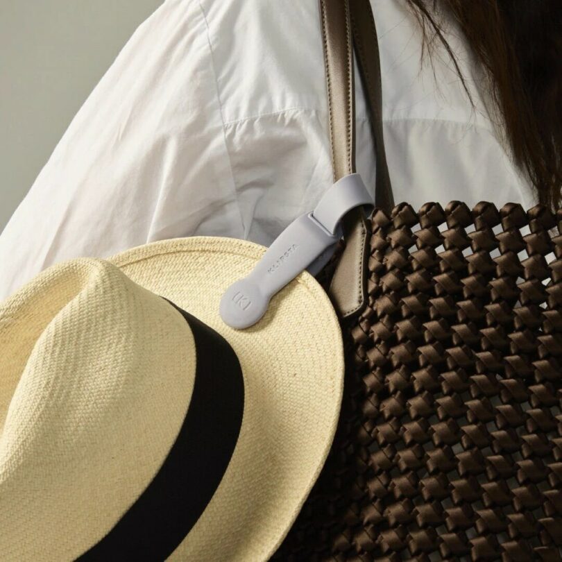 A close-up of a magnetic clip securing a straw hat to a woven brown travel bag.