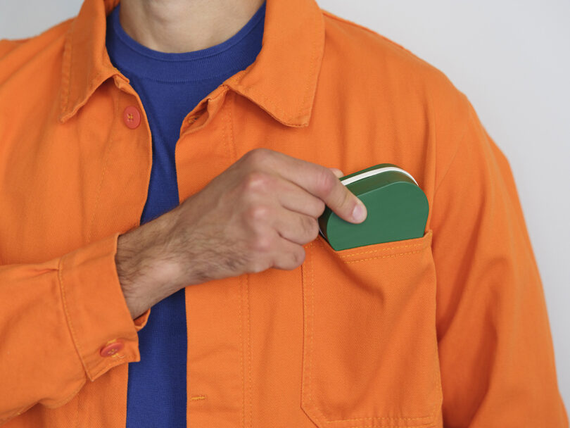 A close-up of a person in an orange jacket sliding a collapsed green Elio bottle into a chest pocket.