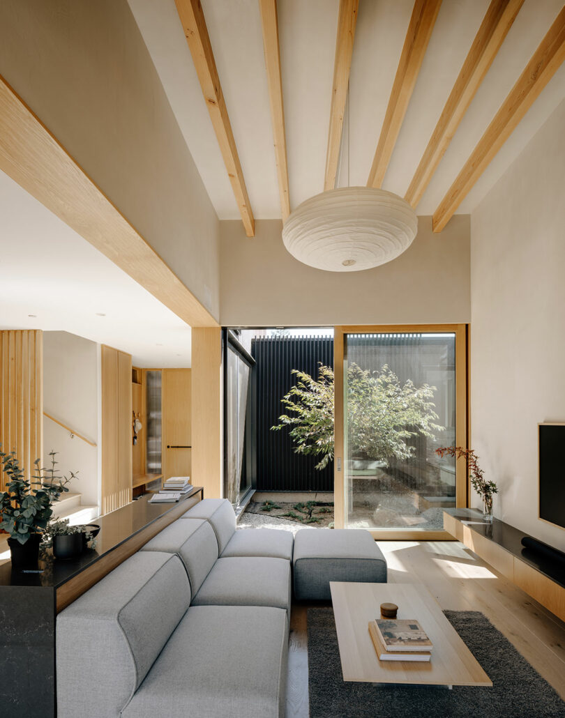 A modern living room with a gray sectional sofa and glass doors opening to a garden.