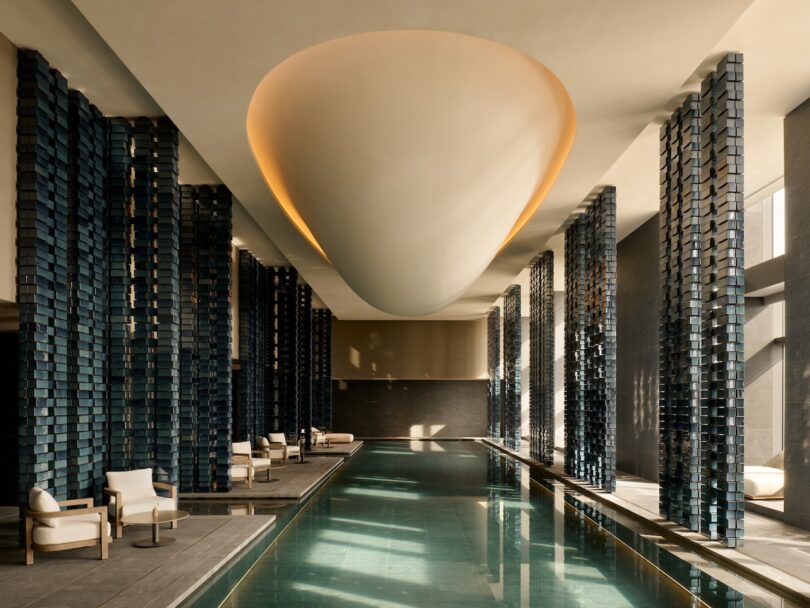 An indoor swimming pool with tall architectural columns and a modern oval ceiling light fixture.