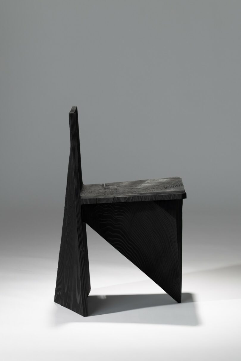 Modern geometric wooden chair with a black finish, shot from a dynamic angle to highlight its sculptural depth.