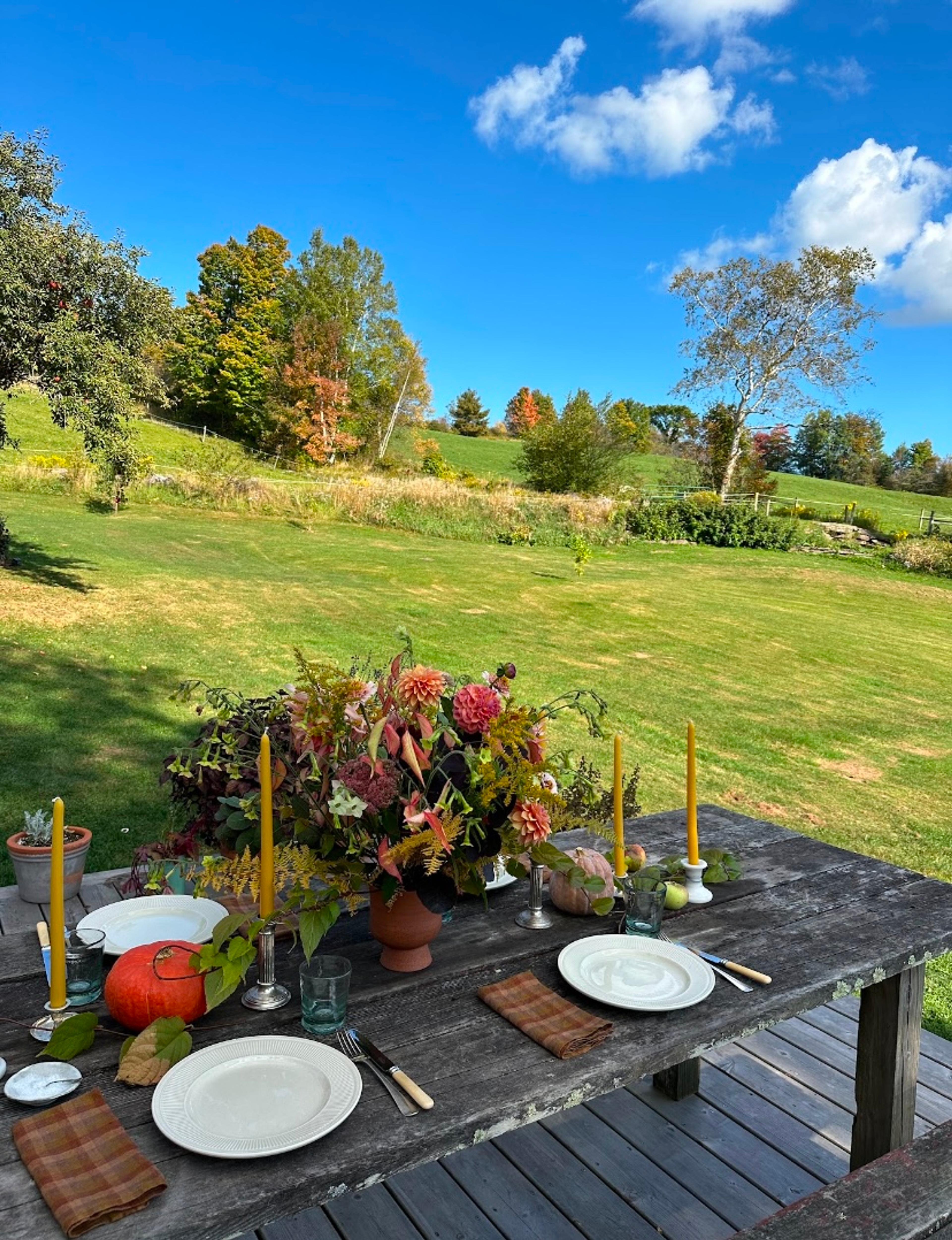 An outdoor dining table decorated with white pumpkins, candles, and scattered autumn flowers.