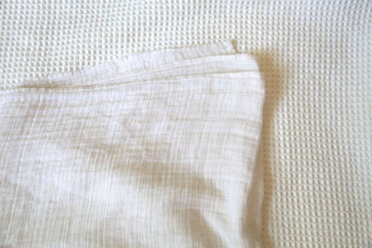A white organic muslin swaddle blanket layered over a chunky waffle weave cotton blanket.