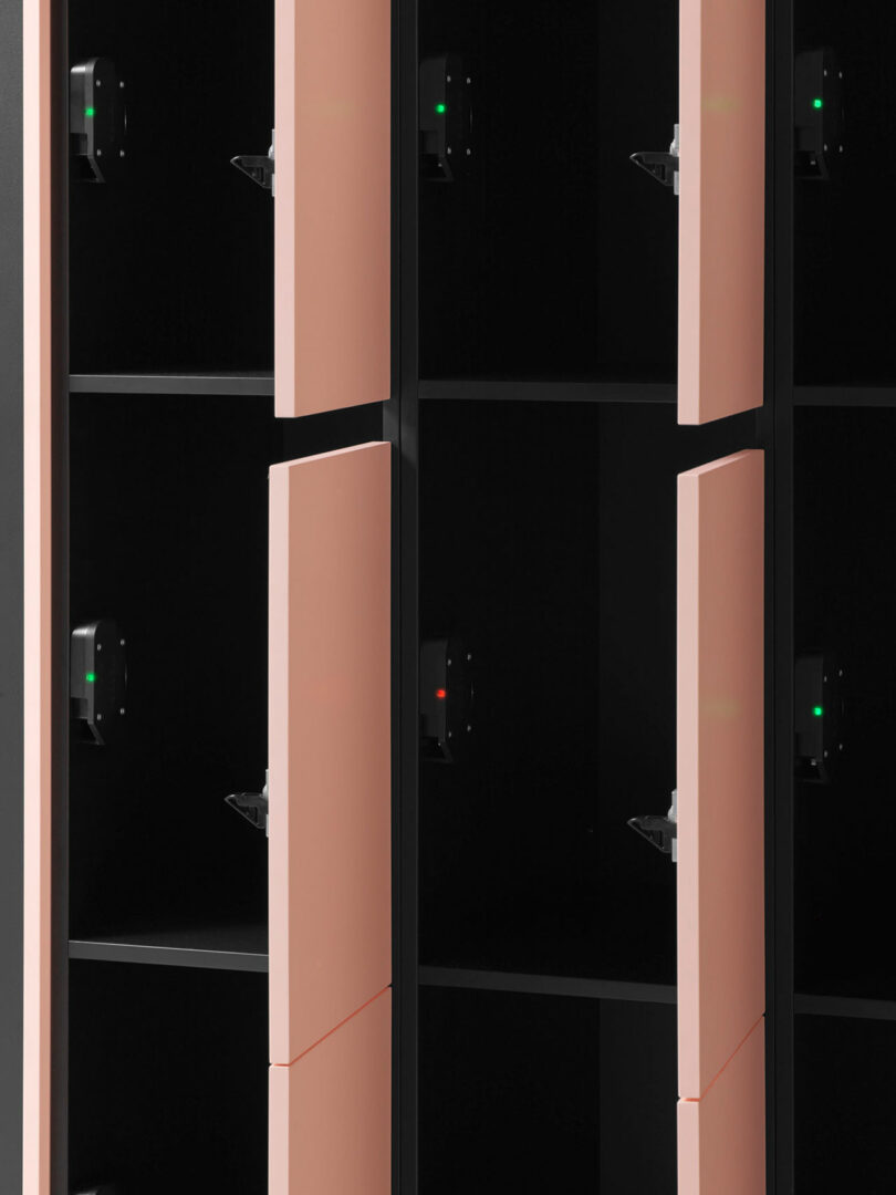 Interior view of open pink lockers showing black compartments, shelves, and internal lighting components.