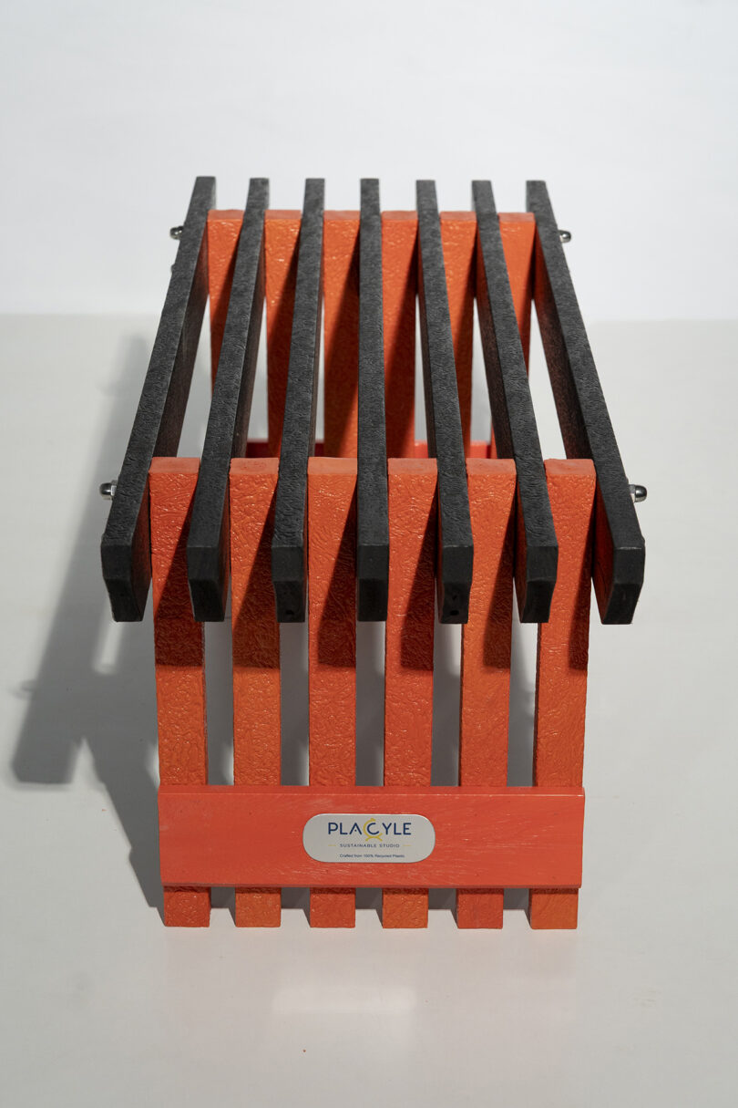 Close-up of the Placycle brand name on the textured surface of a black and orange recycled plastic bench component.