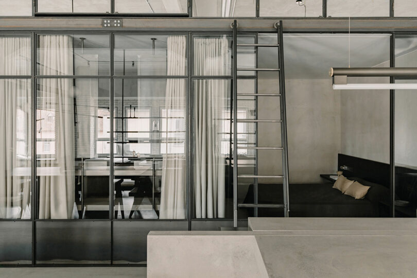 Industrial interior showing glass panels, metal frames, and a ladder leading to a high storage or loft area.