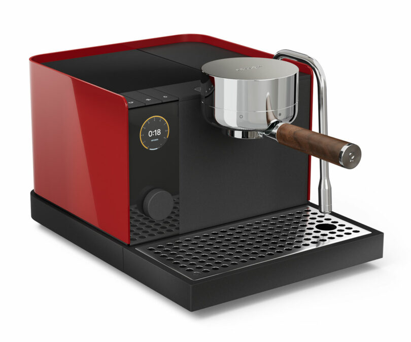 A red and black Fellow espresso machine with wood-handled portafilter on a white background.