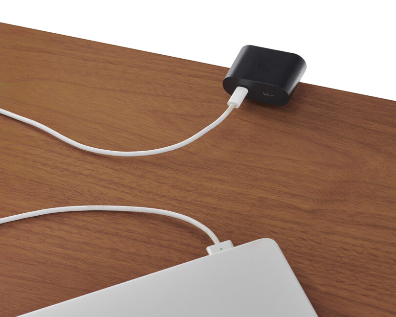 Close-up of a laptop plugged into an integrated USB-C port on a wooden desk surface.