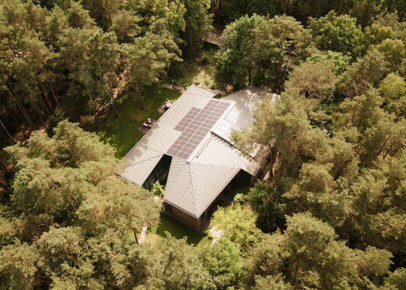 Aerial view of a forest home with solar panels installed on the roof among dense tree coverage.