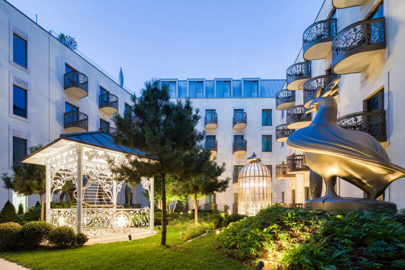 An inner courtyard featuring a large metallic bird sculpture and a decorative gazebo.