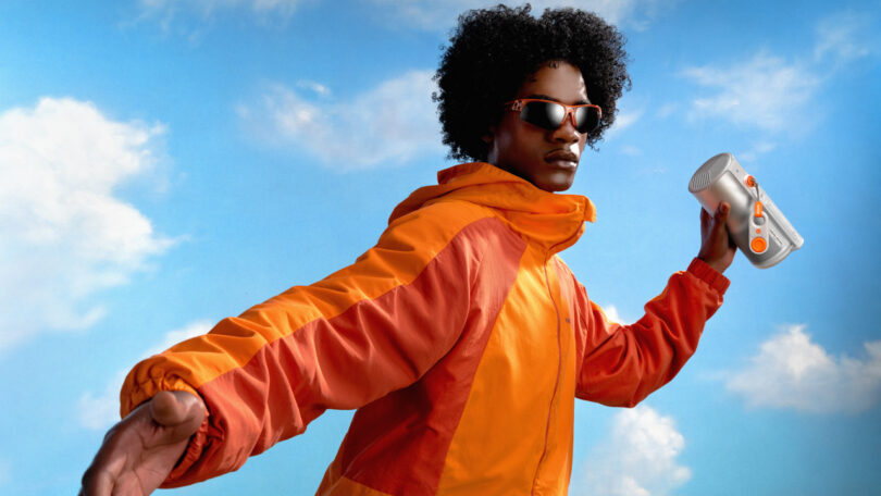 A person in an orange jacket holding the compact XGIMI MoGo 4 against a blue sky.