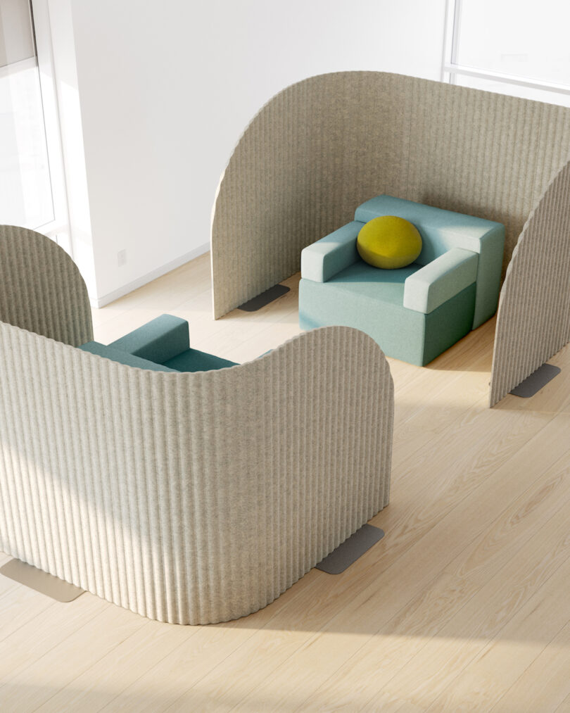 Two teal armchairs enclosed within light grey curved privacy screens on a wood floor.