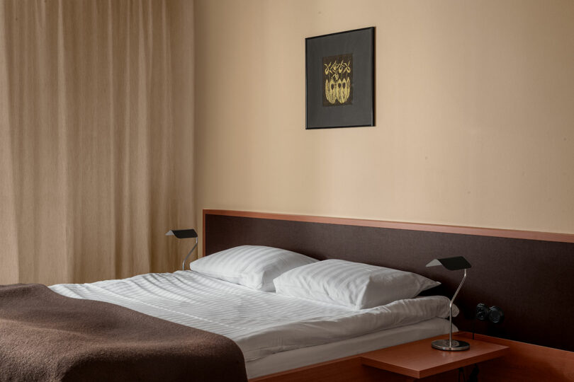 A neatly made bed with white linens and modern black bedside lamps against a neutral wall.