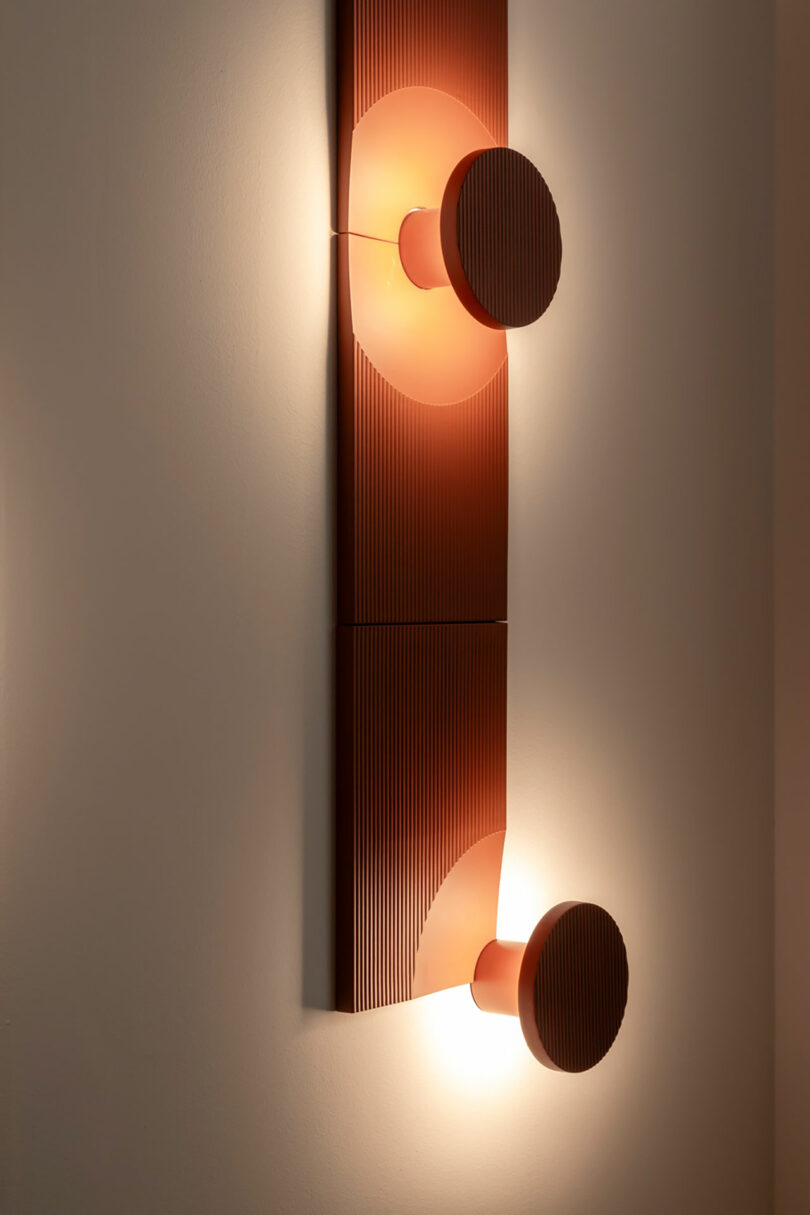 A close-up of a textured red ARID wall light with two circular lamps mounted on a vertical rectangular panel.
