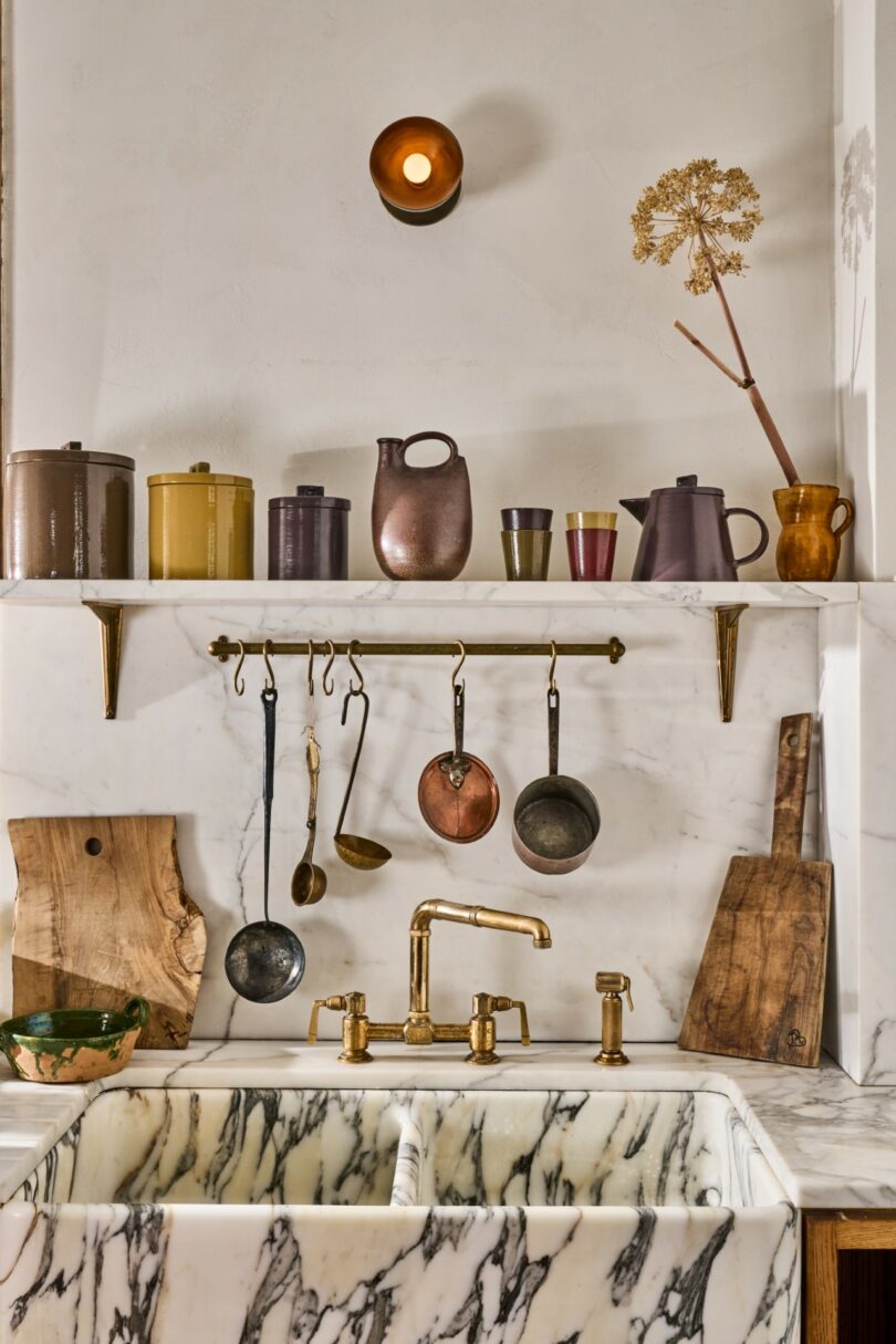 A marble kitchen sink with a brass faucet and ceramic jars arranged on a shelf against a white wall.