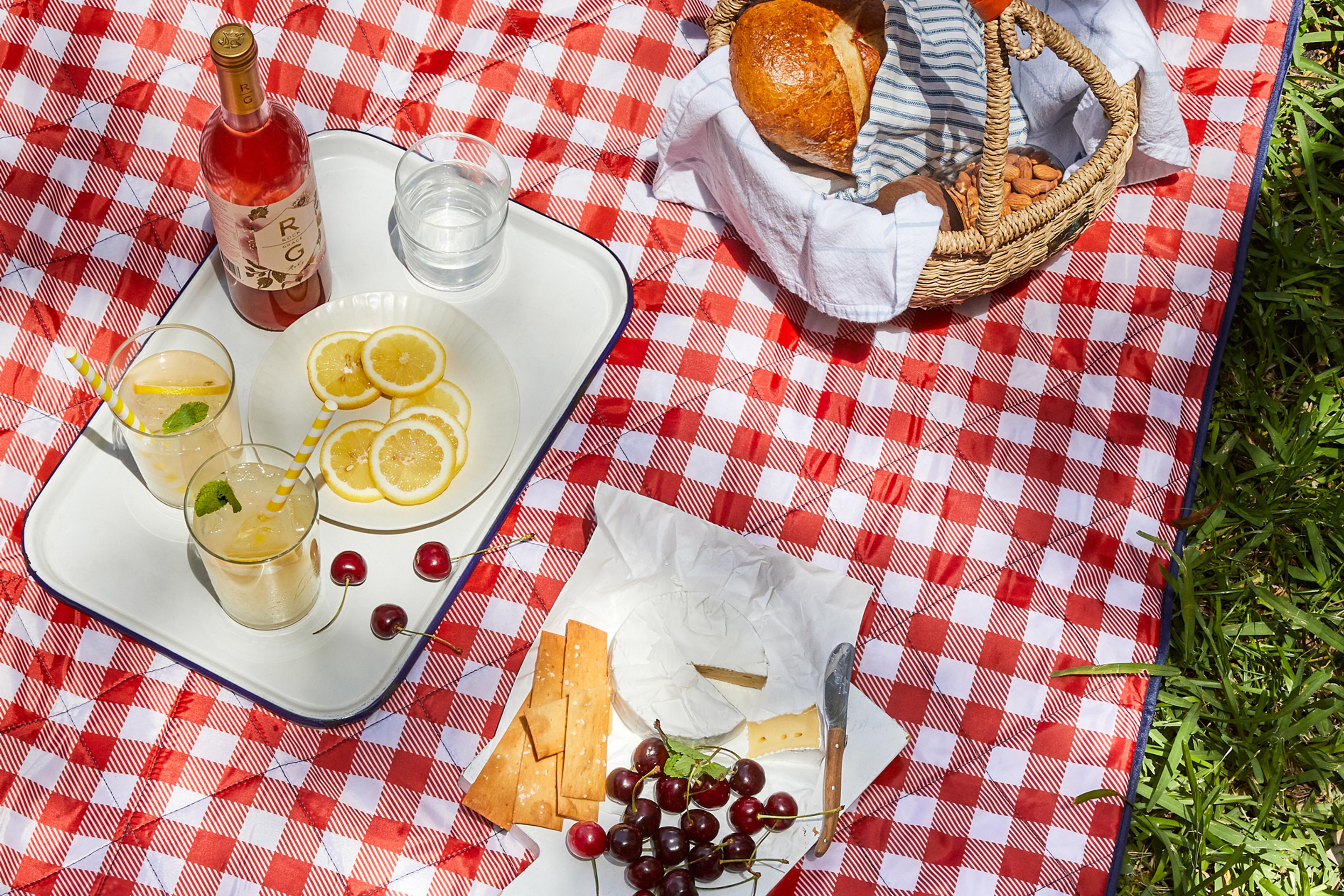 A picnic blanket spread on green grass featuring a charcuterie board and wine glasses.