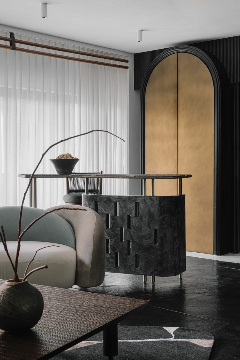 A living area with a curved green sofa, a gold-accented door, and a textured black console table.